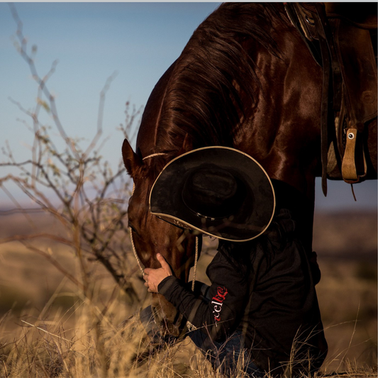 Cowboy kneeling in front of a horse, showcasing the bond between rider and horse during an outdoor western riding experience