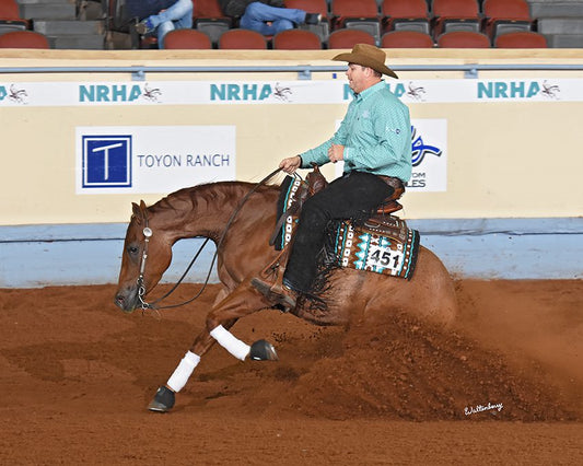 Professional rider Sam Schaffhauser performing a reining slide on a chestnut horse during an NRHA competition, showcasing expert horsemanship and western riding skills