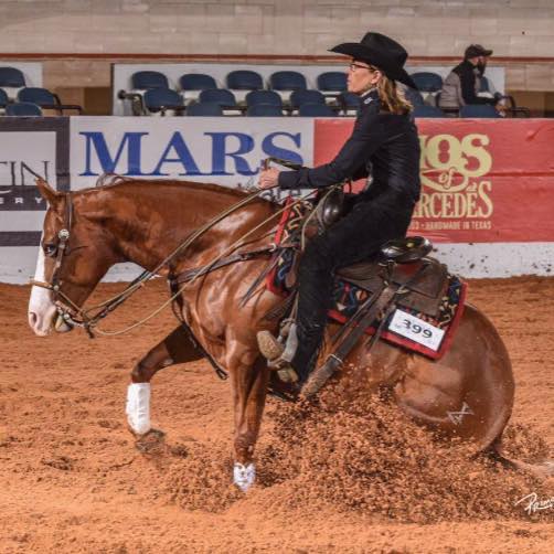 Sponsored rider Carol Metcalf performing a reining slide on a chestnut horse during a professional competition, demonstrating advanced horsemanship and western riding skills